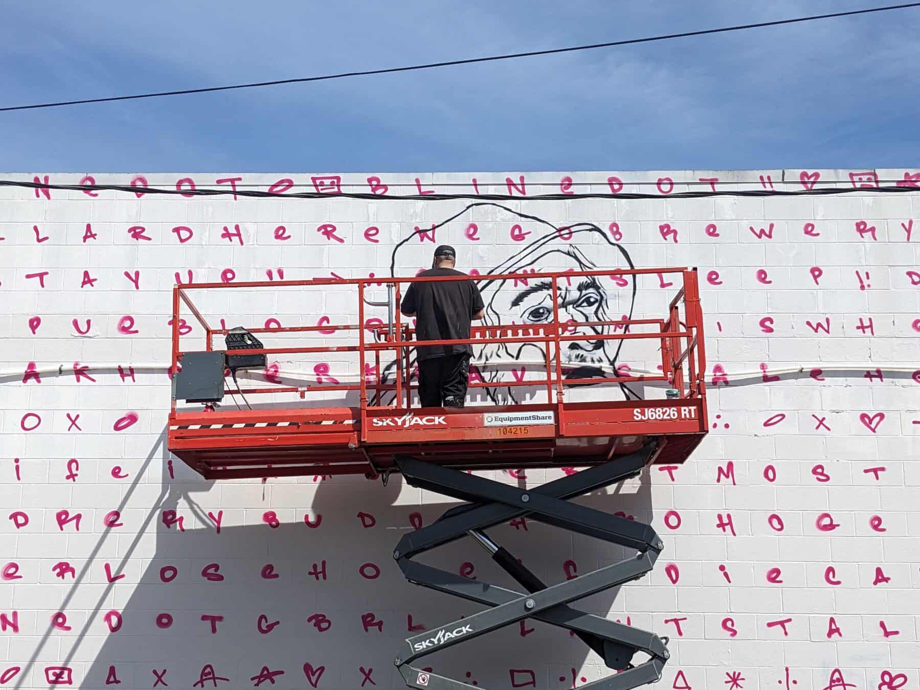 A painter works on a mural on the side of a building.